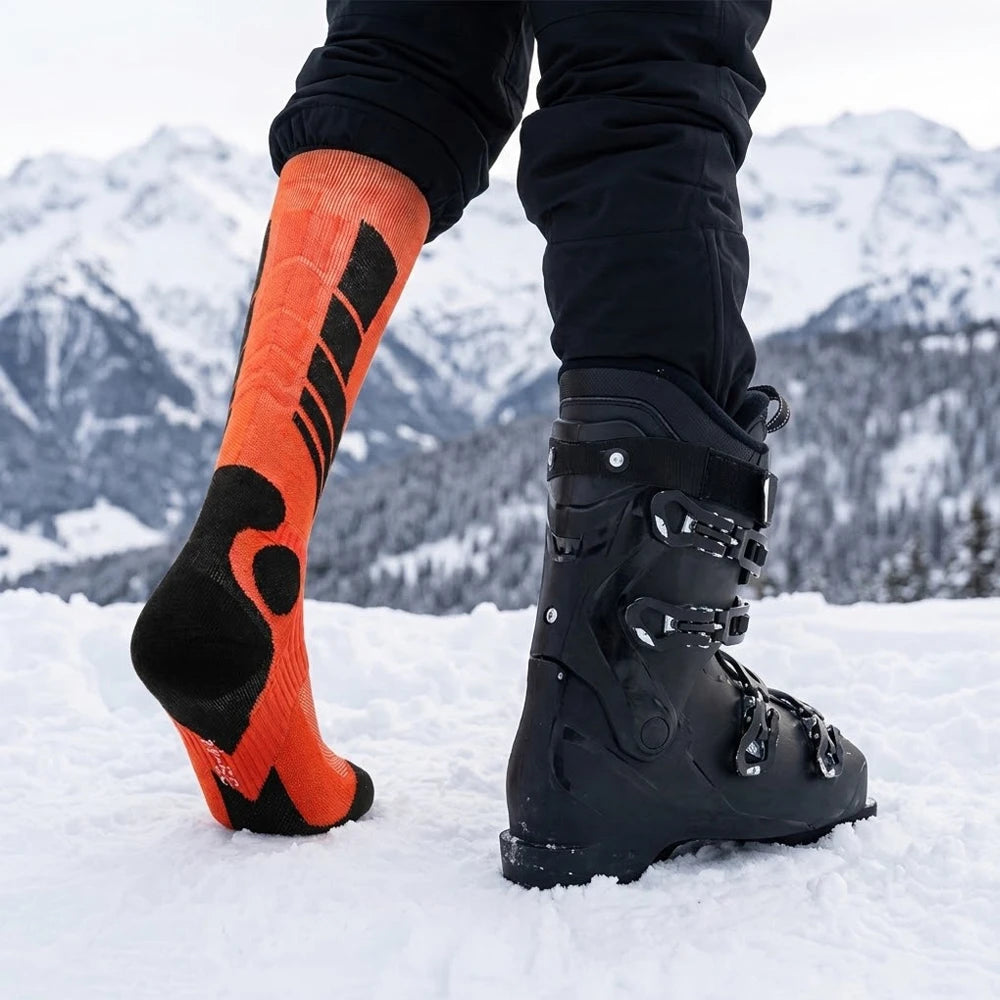 Orange cushioned thermal ski socks shown beside ski boots in the snow
