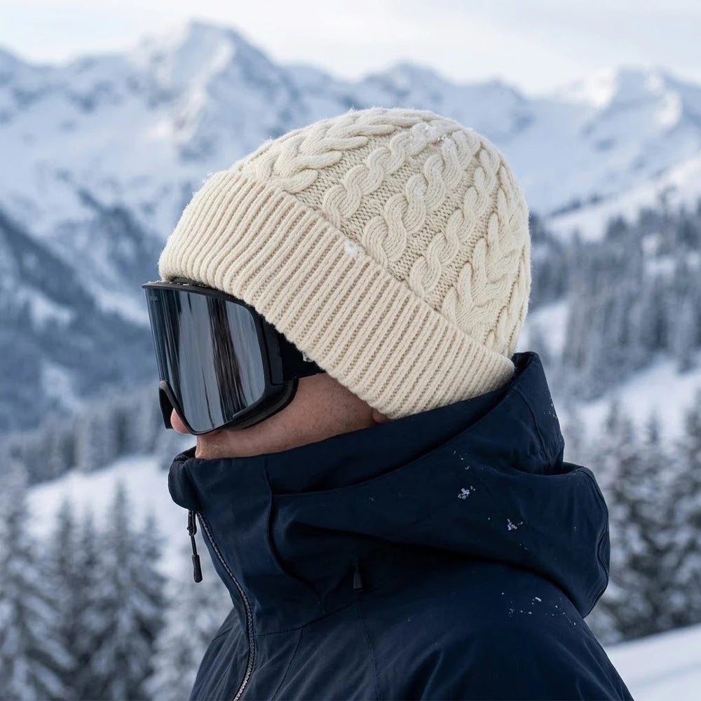 Skier wearing a white cable knit beanie with ski goggles and dark winter jacket.