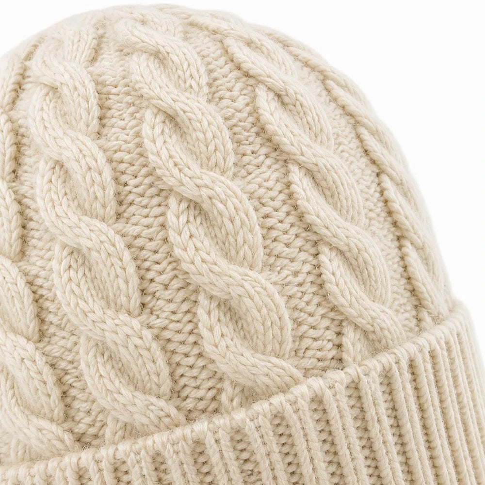 Close-up of the cable knit pattern on a white winter beanie showing detailed texture.