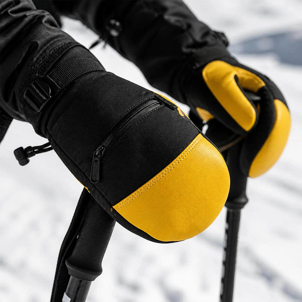 Close-up of black and yellow leather ski mittens holding ski poles in deep snow.